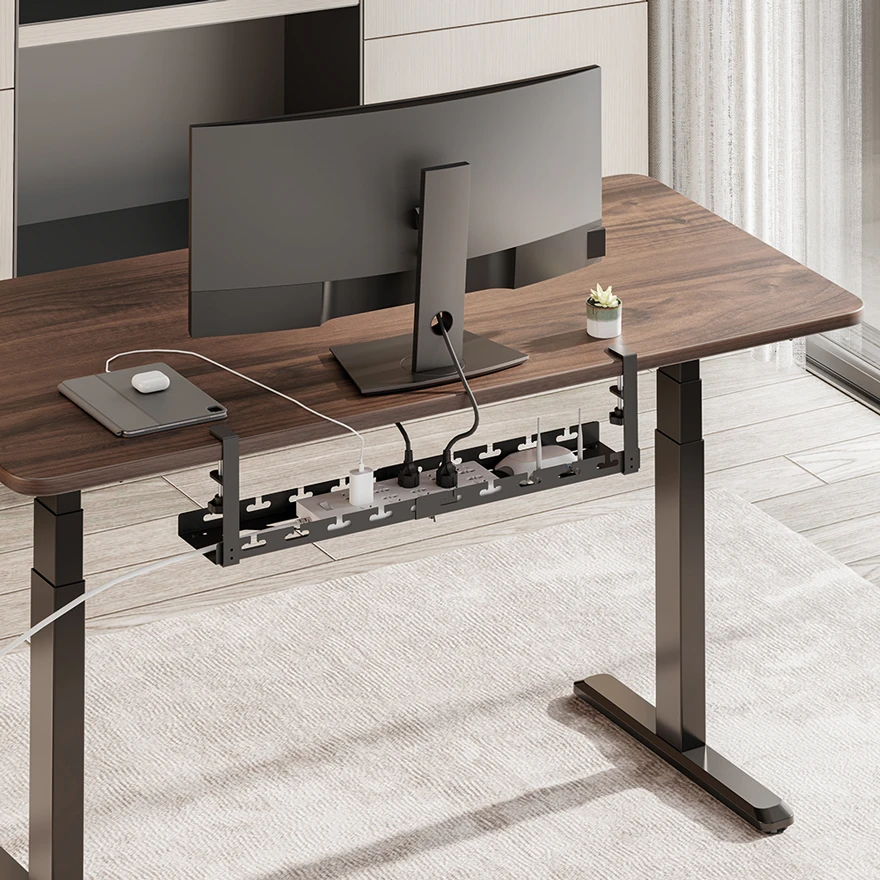 Rear view of a desk with a monitor and a KAB0094 cable tray mounted under the desktop, holding a power strip and cables